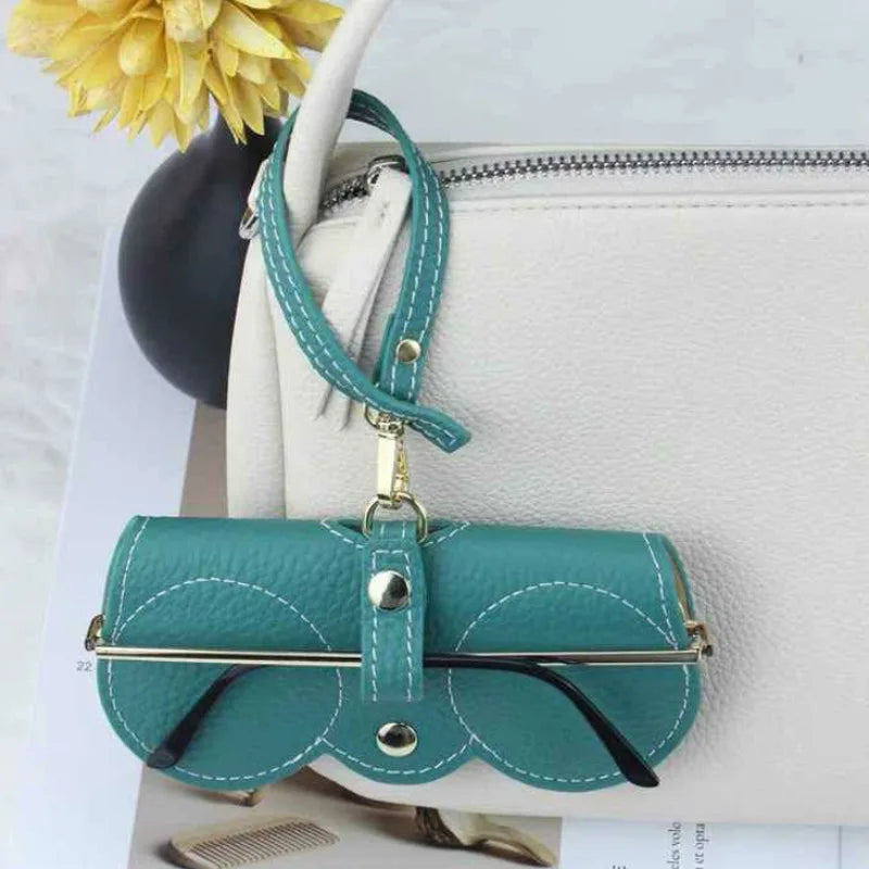 A teal leather pouch with a gold clasp and strap is displayed on a white handbag.