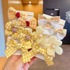 A hand holds a set of yellow and white checkered fabric flower bow hair ties for girls.