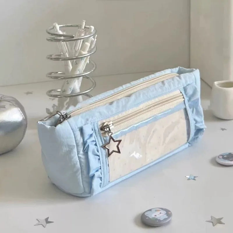 A light blue lace pencil case is shown next to a silver pen holder and small decorative stars on a white surface.
