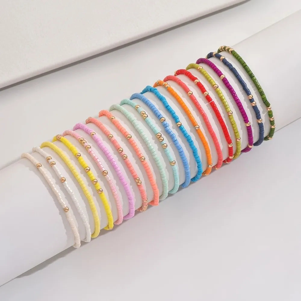 A stack of colorful beaded bangles in various shades of pink, orange, yellow, green, and blue worn on a wrist.