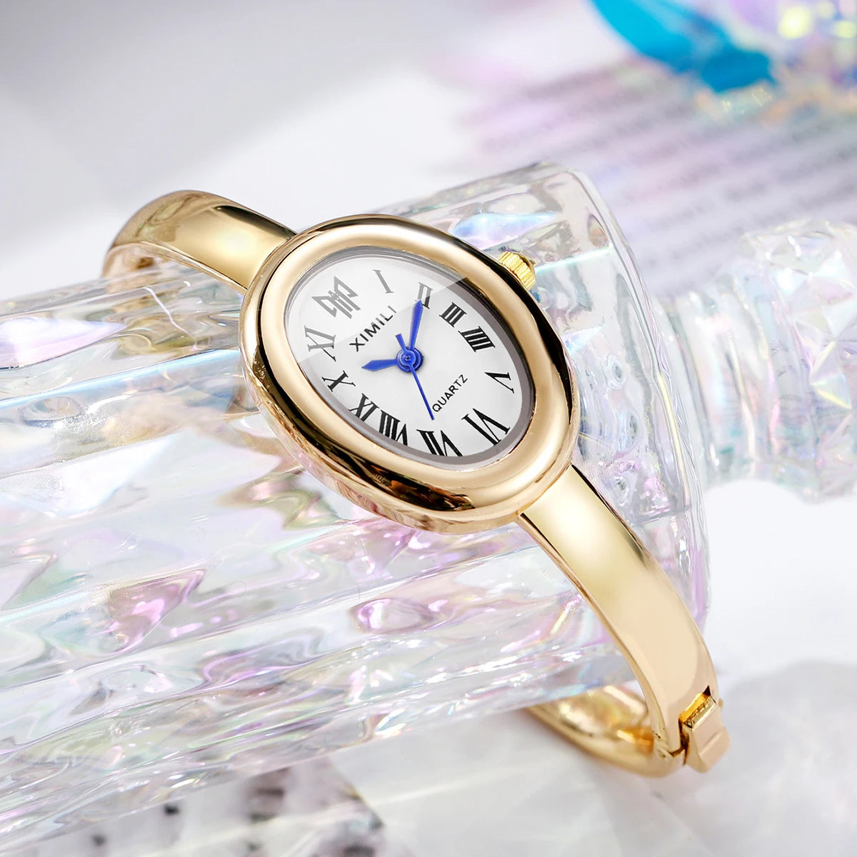 A gold-toned quartz watch with a blue dial and Roman numerals is displayed on a clear, textured glass surface.