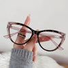 Eine Hand hält eine Vintage-Cat-Eye-Lesebrille mit braunen und rosa Rahmen vor weißem Hintergrund.