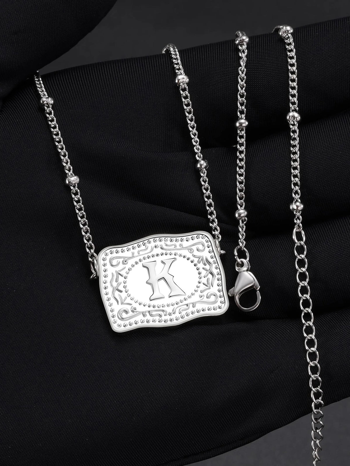 Silver initial letter pendant necklace with a chain and bail displayed on a black fabric background