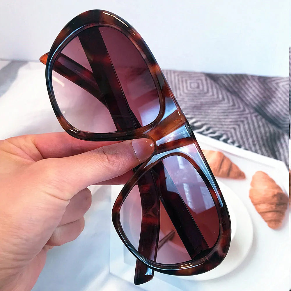 A hand holds a pair of vintage gradient leopard print sunglasses with brown and amber lenses.