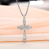 A silver cross pendant necklace with a detailed design is displayed on a pink fabric background.