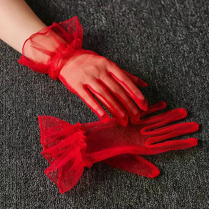 A pair of sheer red lace tulle finger gloves resting on a dark gray fabric.