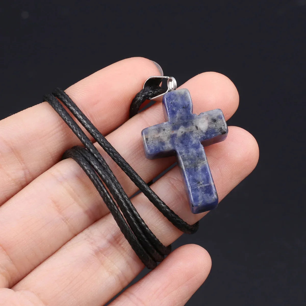 Eine Hand hält eine Tigerauge-Agat-Kreuz-Anhänger-Kette mit schwarzem Schnur und silberner Schnalle.