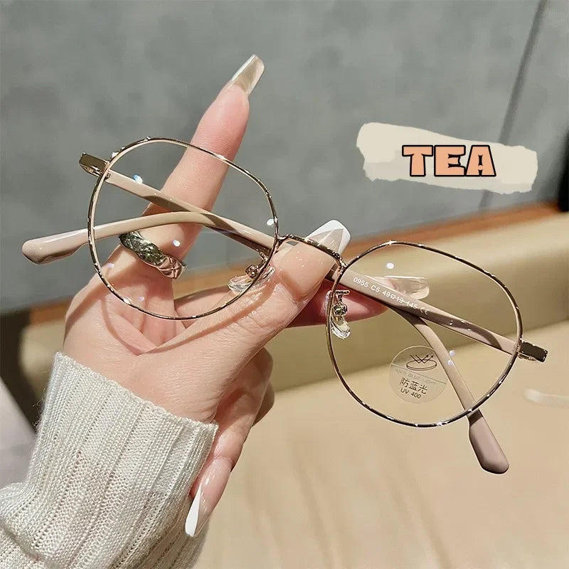 Une main tient une paire de lunettes fines à monture ronde rose pâle et transparente sur un fond neutre.