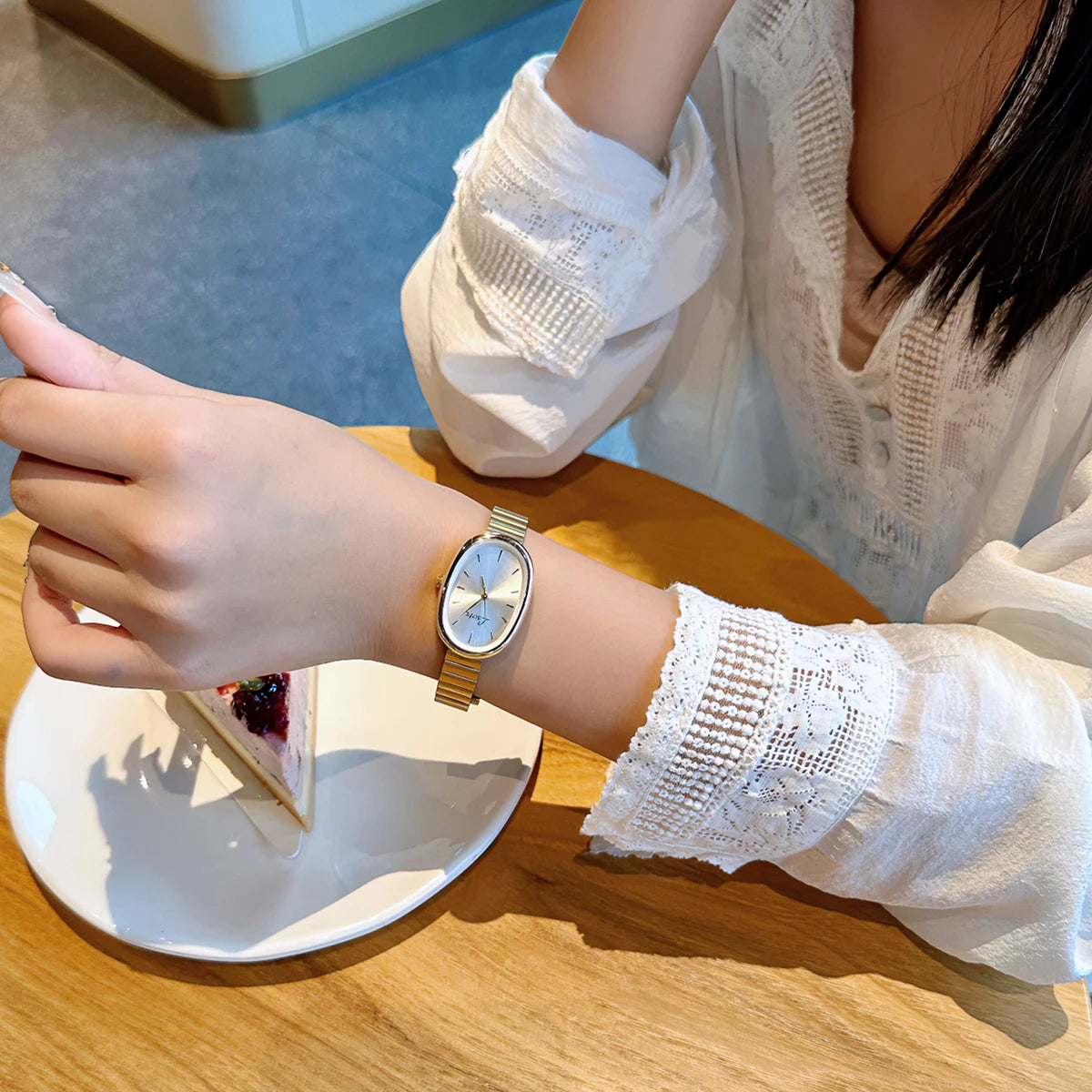 Une main portant une élégante montre en quartz avec un bracelet doré tient une part de gâteau sur une table en bois.