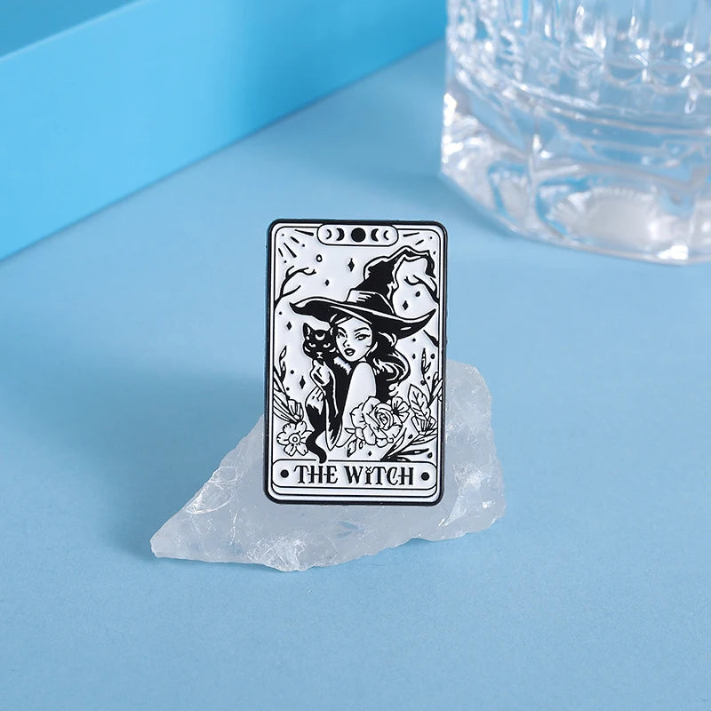 A black tarot card featuring a witch in a hat is displayed on a light blue surface next to a piece of clear ice.