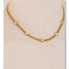 A close-up of a gold-toned stainless steel charm necklace featuring small clear cubic zirconia stones.