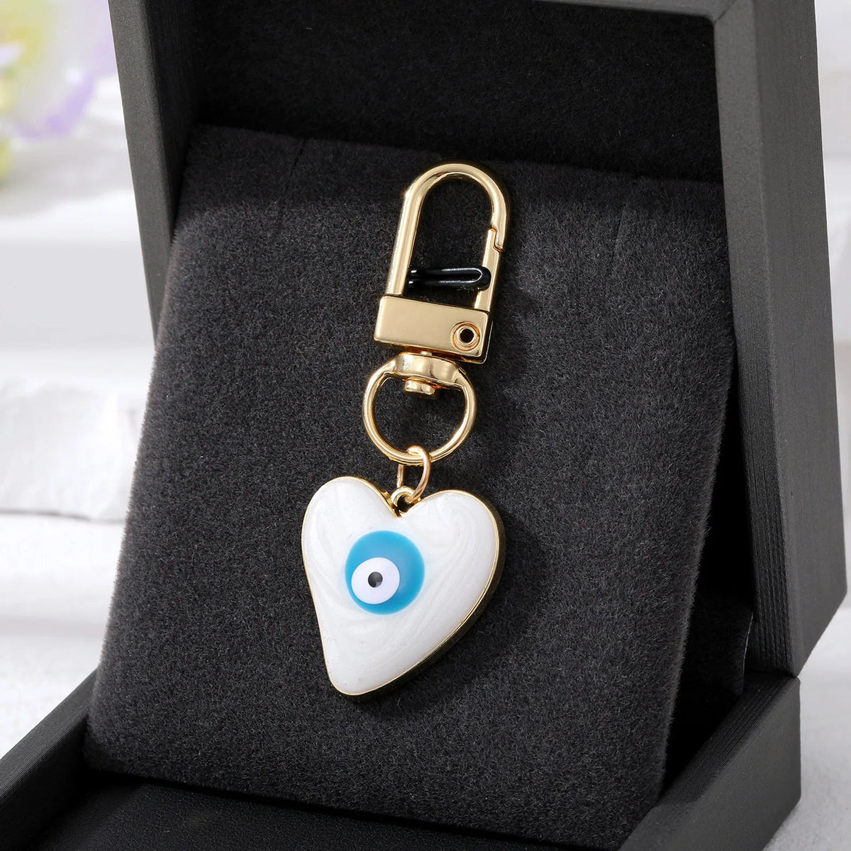 Gold heart-shaped keychain with a white and blue evil eye design displayed in a black velvet box.