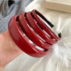 A hand holds a stack of glossy red PU leather fashion headbands against a light fabric background.