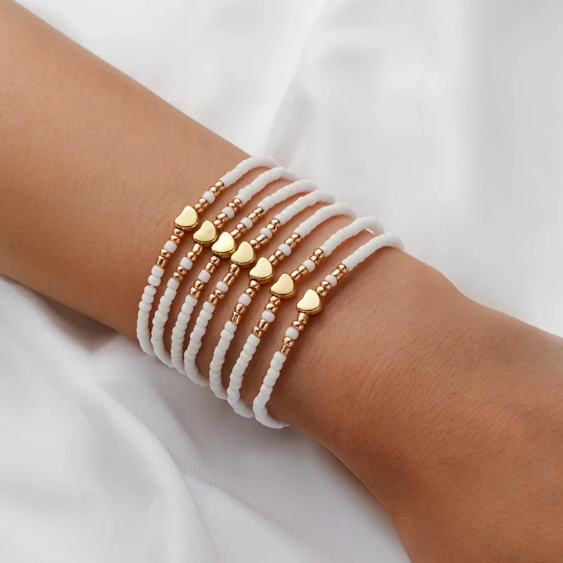 A set of white and gold resin beaded bracelets stacked on a person's wrist.