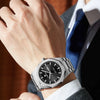 A close-up of a stainless steel luminous quartz watch worn on a wrist, displayed against a suit jacket.