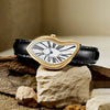 A gold-toned fashion quartz wristwatch with a white Roman dial and blue accents rests on rough, natural stones.