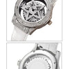 A close-up of a silver watch with a diamond-encrusted rotating star design on the face and a white leather strap.