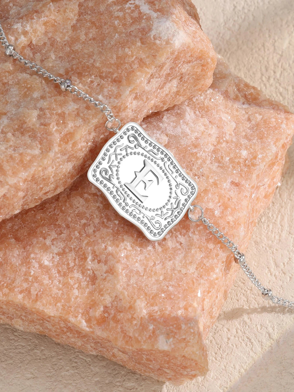 Silver pendant necklace with an engraved letter E on a pink quartz stone background.