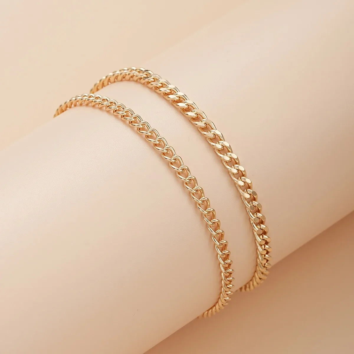 Gold plated minimalist Cuban link anklets worn on a person's ankle.
