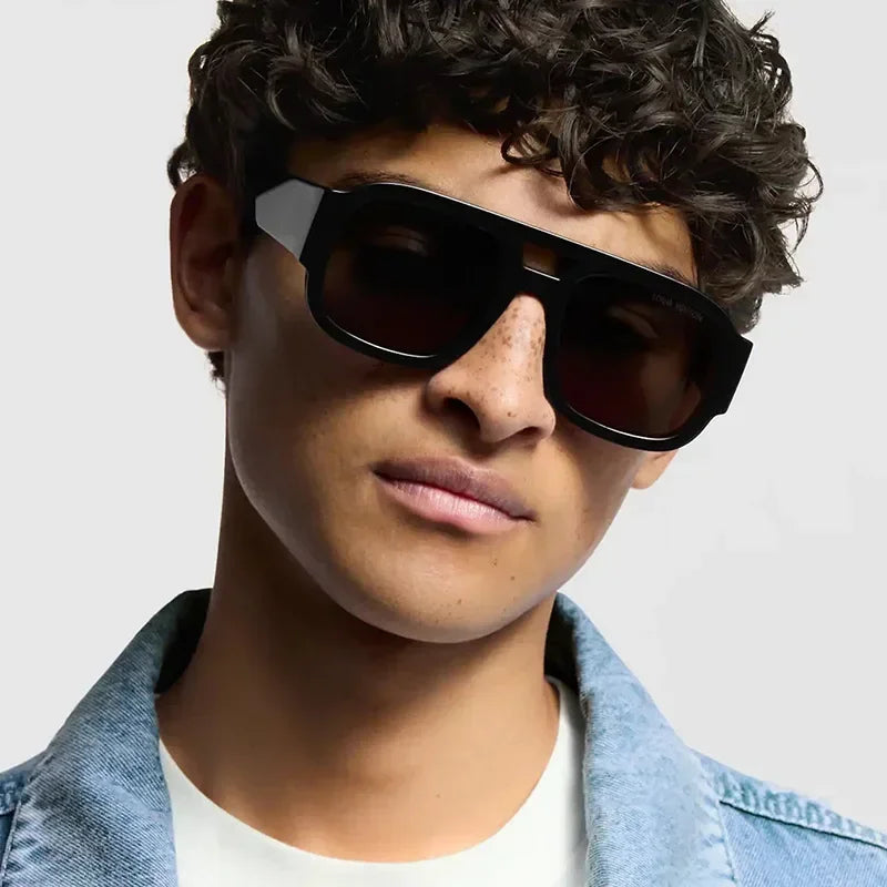 Modelo masculino vistiendo gafas de sol cuadradas retro de doble puente negras y una chaqueta de mezclilla.