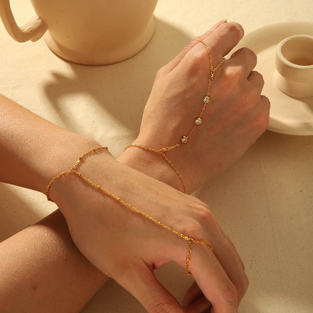 A close-up of a hand wearing an 18K gold plated stainless steel zircon ring bracelet on a light-colored surface.