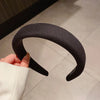 Une main tient un bandeau pour cheveux noir épaissi, montrant sa forme incurvée sur un fond clair.