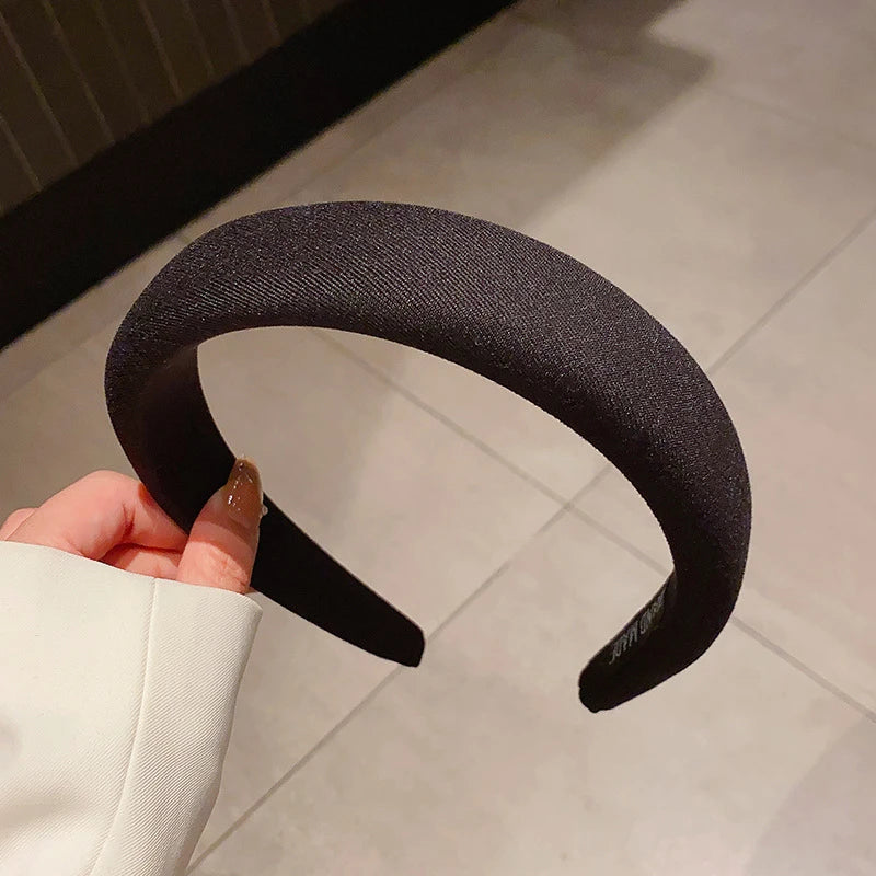 Une main tient un bandeau pour cheveux noir épaissi, montrant sa forme incurvée sur un fond clair.