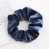 A close-up of a dark blue velvet scrunchie with gathered fabric texture resting on a white background.
