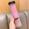 Un contenedor de plástico transparente lleno de gomas para el pelo con rayas onduladas rosadas, sostenido por una mano.