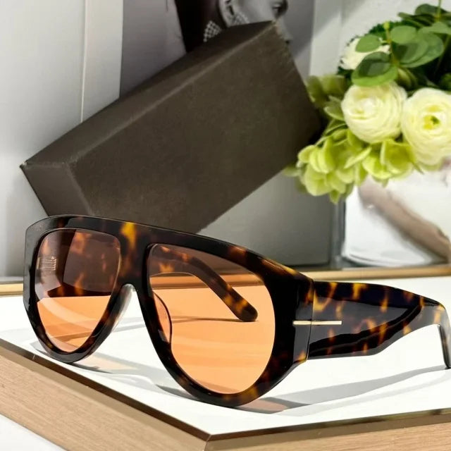Brown leopard print sunglasses resting on a wooden surface next to a green floral arrangement.