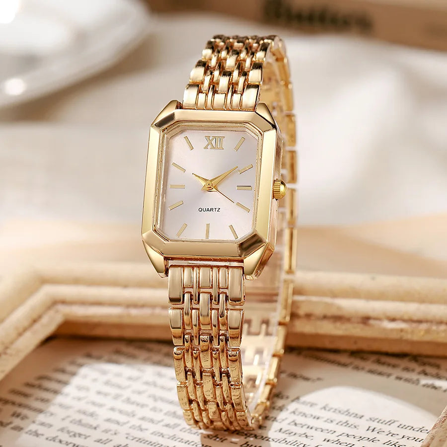 A gold minimalist quartz watch with a square face and gold-toned bracelet resting on a wooden surface.