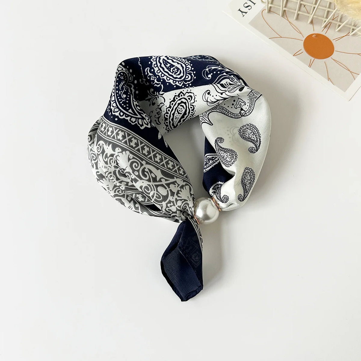 A dark blue and white silk scarf featuring a detailed print tied with a satin fold and a pearl bead.
