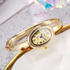 A gold-toned quartz watch bracelet with a round face and Roman numerals is displayed on a white surface.