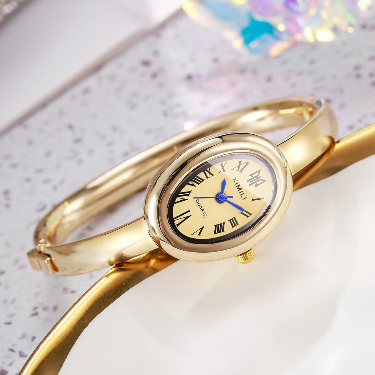 A gold-toned quartz watch bracelet with a round face and Roman numerals is displayed on a white surface.