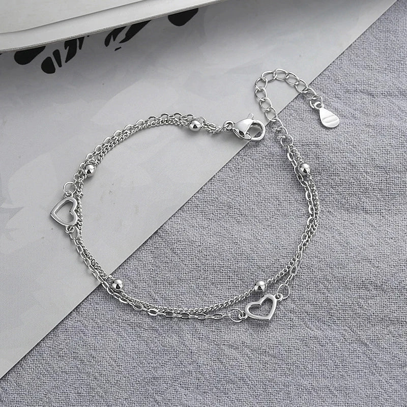 A sterling silver double heart charm bracelet laid on a gray fabric background.