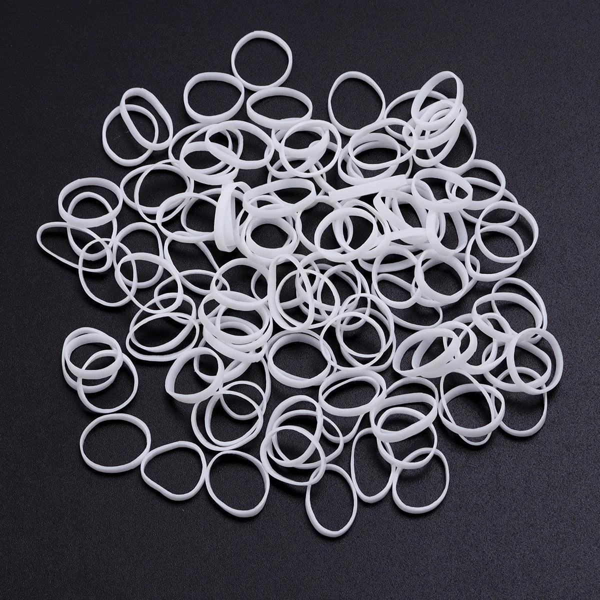 A pile of white elastic hair ties or rings scattered on a dark surface.