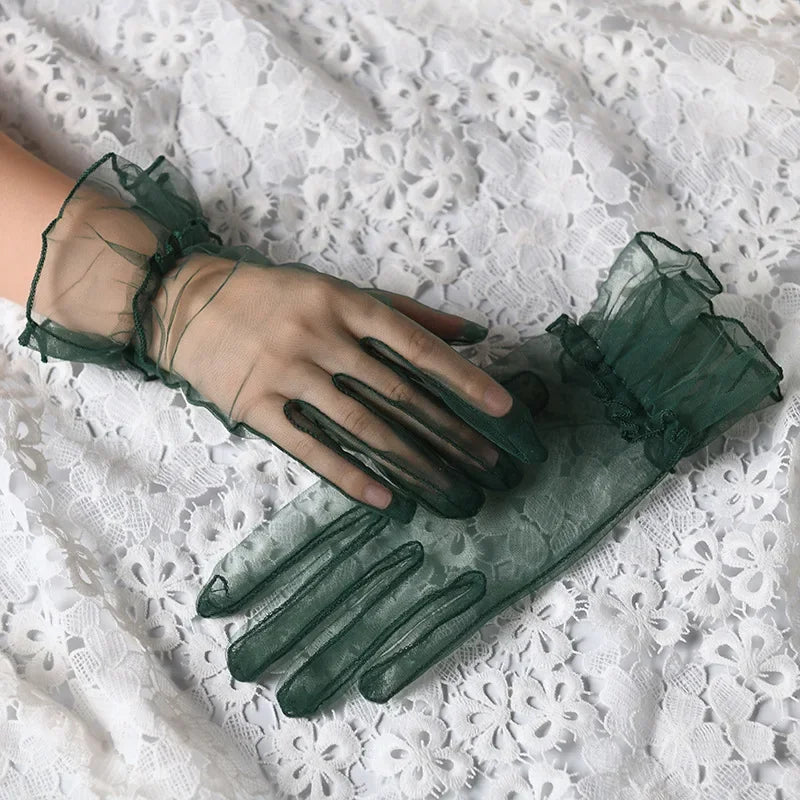 A hand wearing sheer green lace tulle finger gloves resting on white lace fabric.