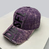 A purple embroidered letter baseball cap with black lettering and distressed fabric resting on a white surface.