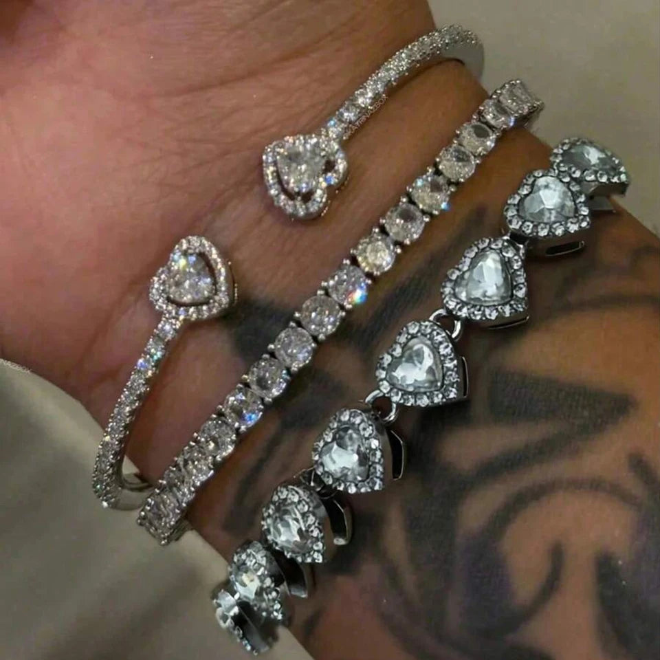 A close-up of a hand wearing a set of geometric rhinestone heart stacking bracelets on the wrist.