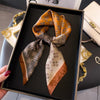 A luxury silk scarf in shades of brown and gold is displayed in a black frame.