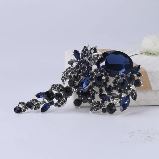 Un amas de fleurs de cristal bleu foncé et noir et une grande broche saphir sur une surface blanche.