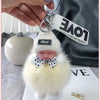 A white knitted plush doll with a pink face and a bow, attached to a silver keychain.