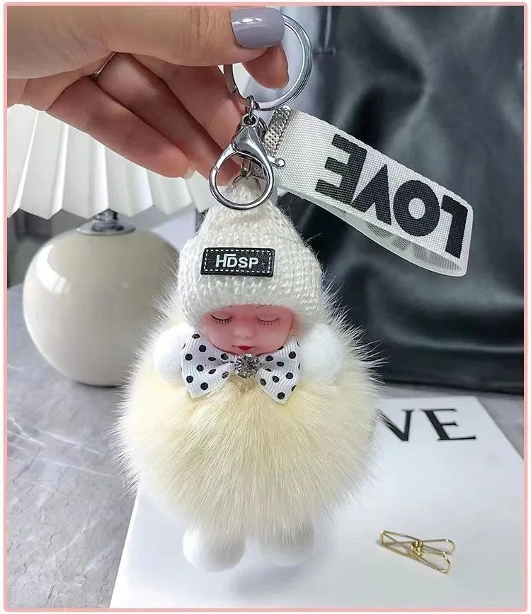 A white knitted plush doll with a pink face and a bow, attached to a silver keychain.