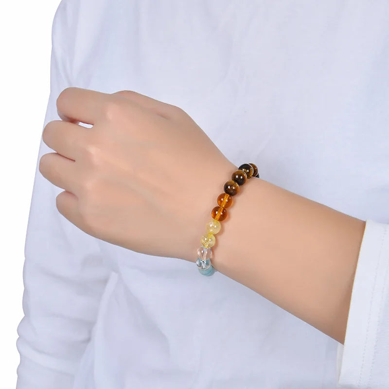 A wrist wearing a Tiger Eye crystal bracelet with various colored beads against a white shirt background.