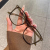 A hand holds a pair of brown-framed anti-blue light eyeglasses against a neutral background.