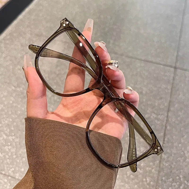A hand holds a pair of brown-framed anti-blue light eyeglasses against a neutral background.