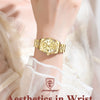 A close-up of a gold-toned ladies wristwatch worn on a wrist, set against a soft, light background.