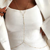 A close-up of a woman wearing a delicate gold belly chain body jewelry necklace under a white blazer.