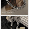 A close-up of a stainless steel NK chain necklace draped over dark fabric and next to a light-colored sculpture.