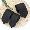 A stack of classic solid black neckties resting on a woven natural fiber mat.